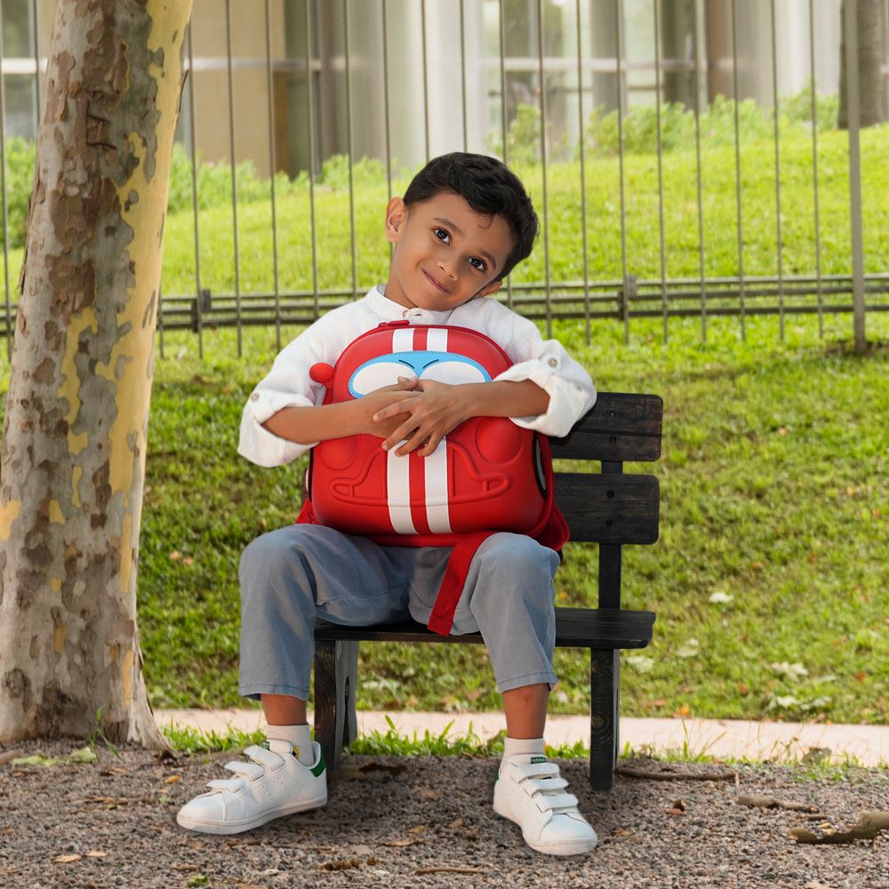 Boy sitting outdoors on a park bench, wearing the Bentotss Race Ready Red Bento Bag backpack